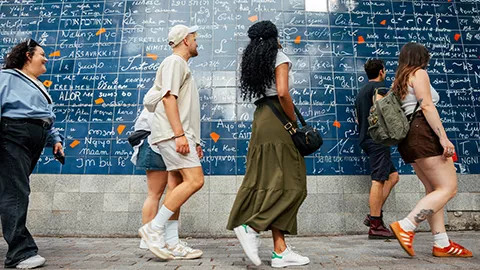 People walking past a blue tiled wall with white writing in Paris.