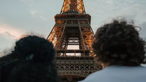 The back of two people sitting side by side with the Eiffel Tower in focus in front of them.
