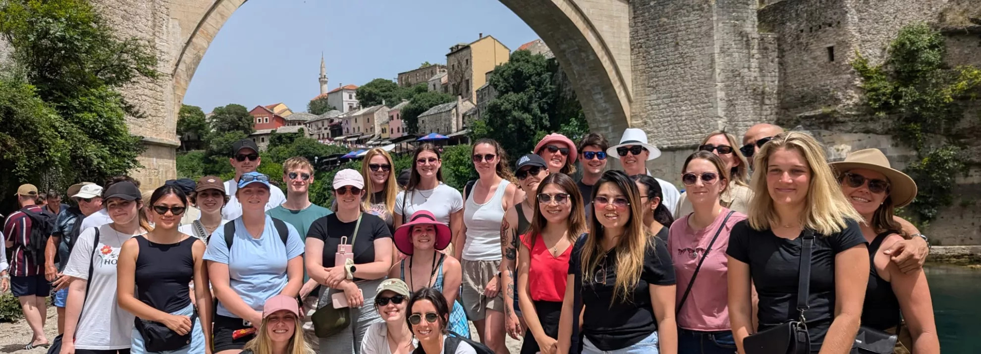 A group of topdeckers standing in front of an old bridge 