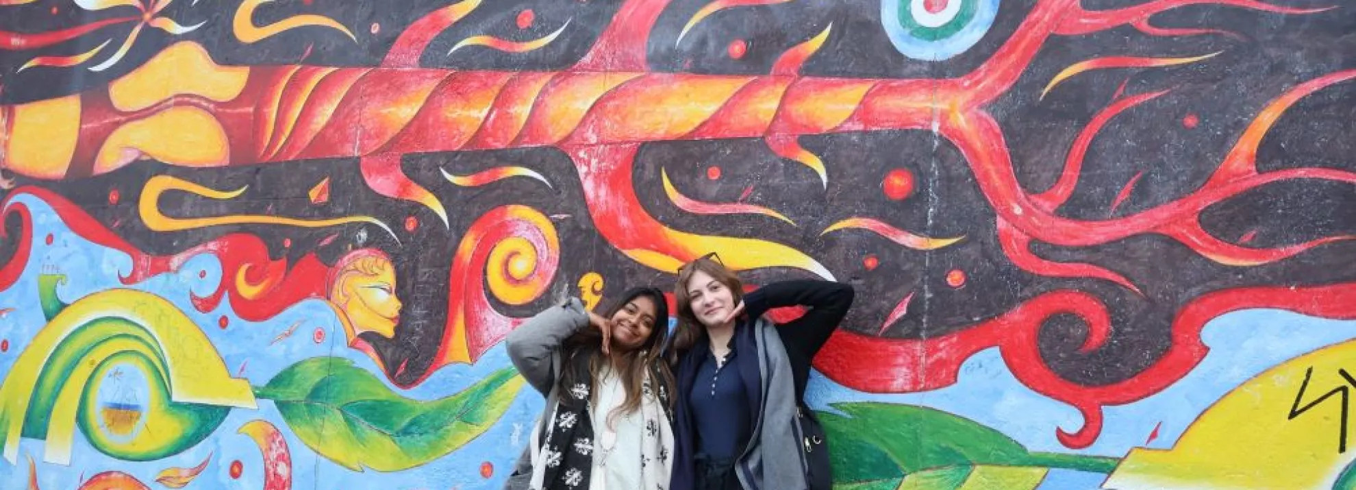 Two women standing in front of a wall of painted art