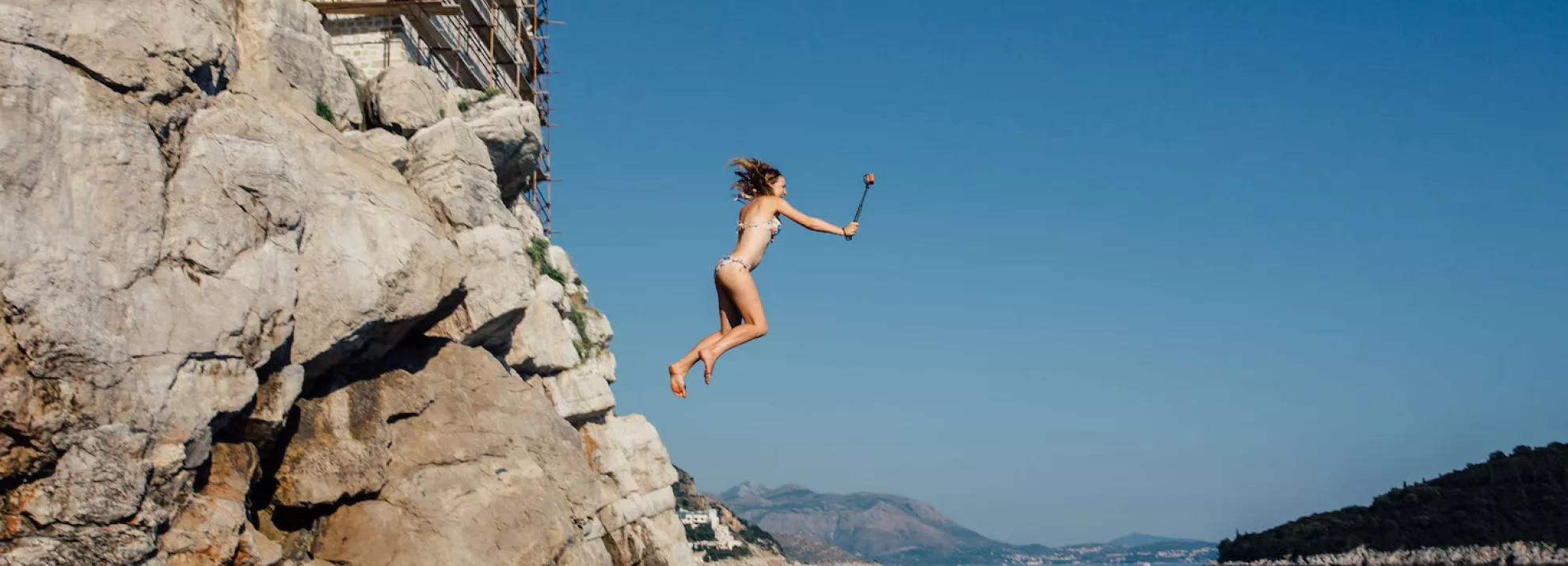 woman jumping off rocks into water