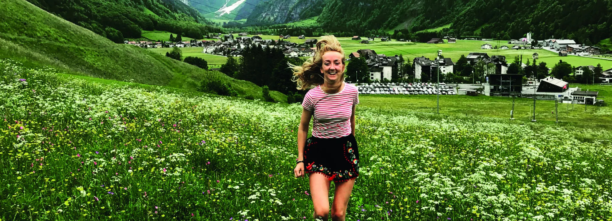 A woman running through a field of flowers, with Swiss mountains in the background