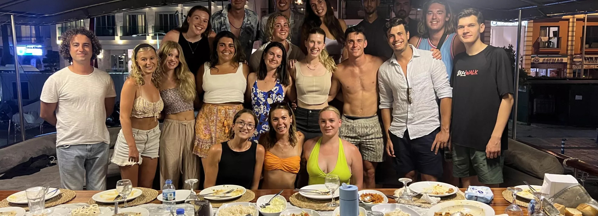 large group of people smiling and standing behind a table of food