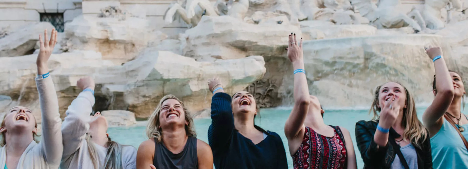 Happy group of people throwing a coin behind them into the Trevi Fountain