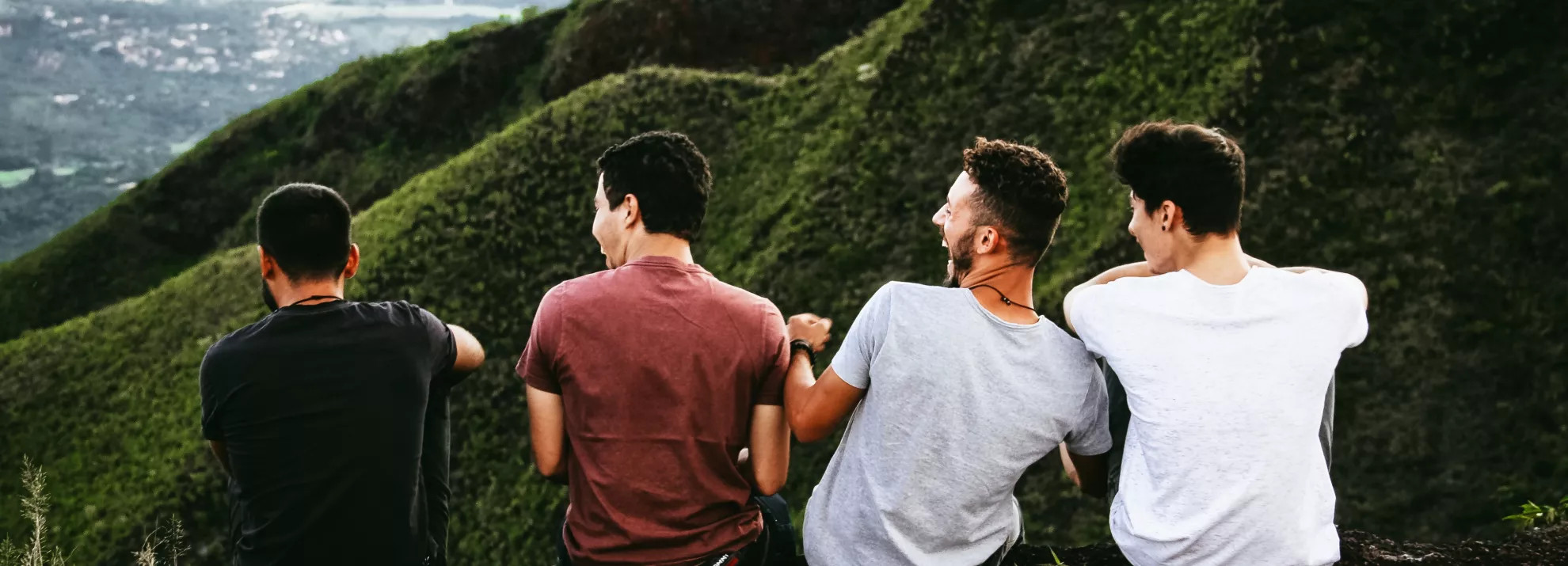 four men sitting away from the camera laughing. They are sat on a mountain