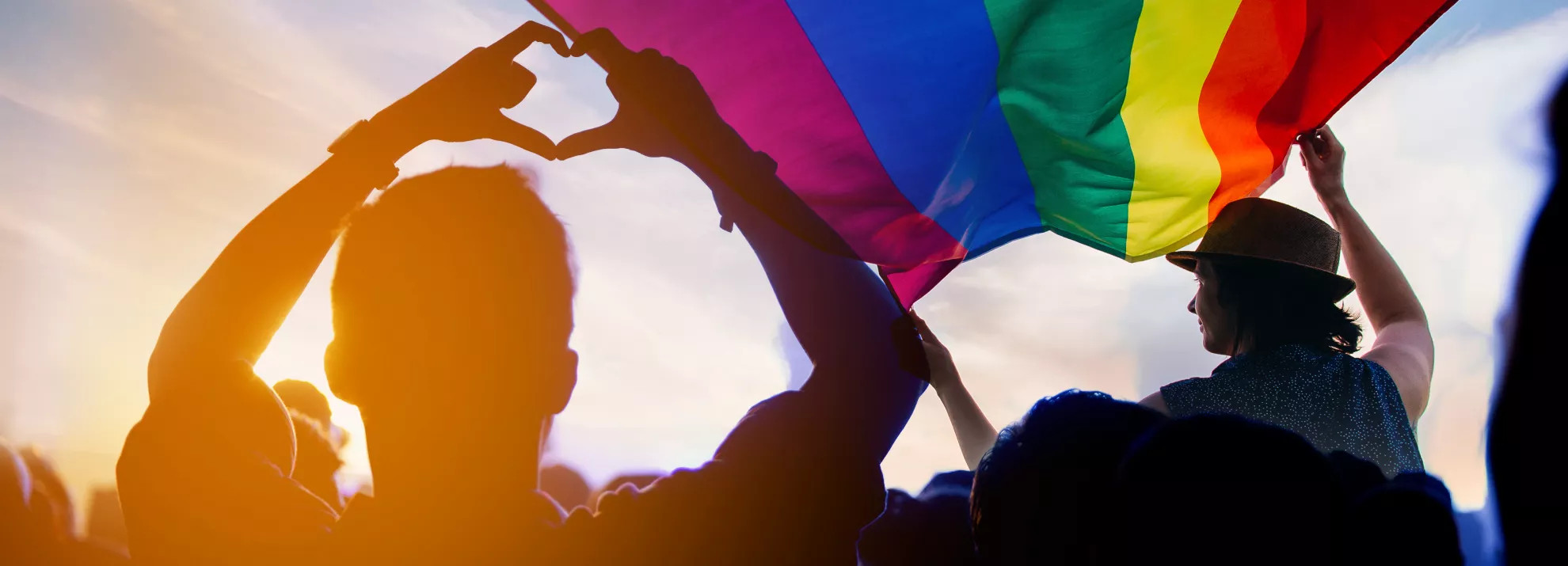 A silhouette of a crowd with a pride flag in the sky