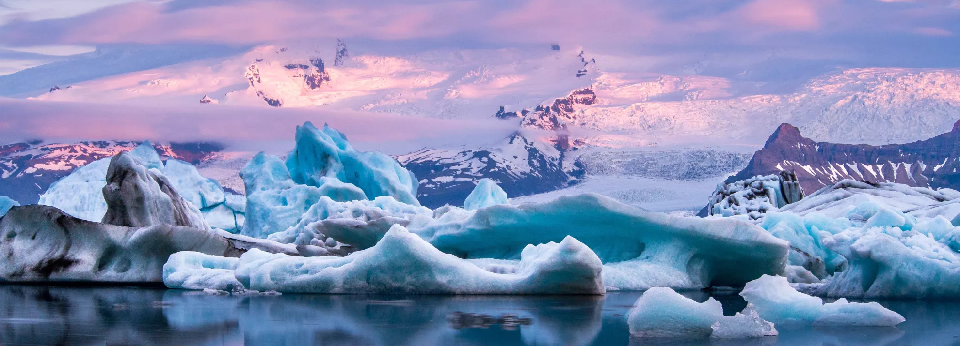 An orange and pink sunset over snow, ice and water in Iceland