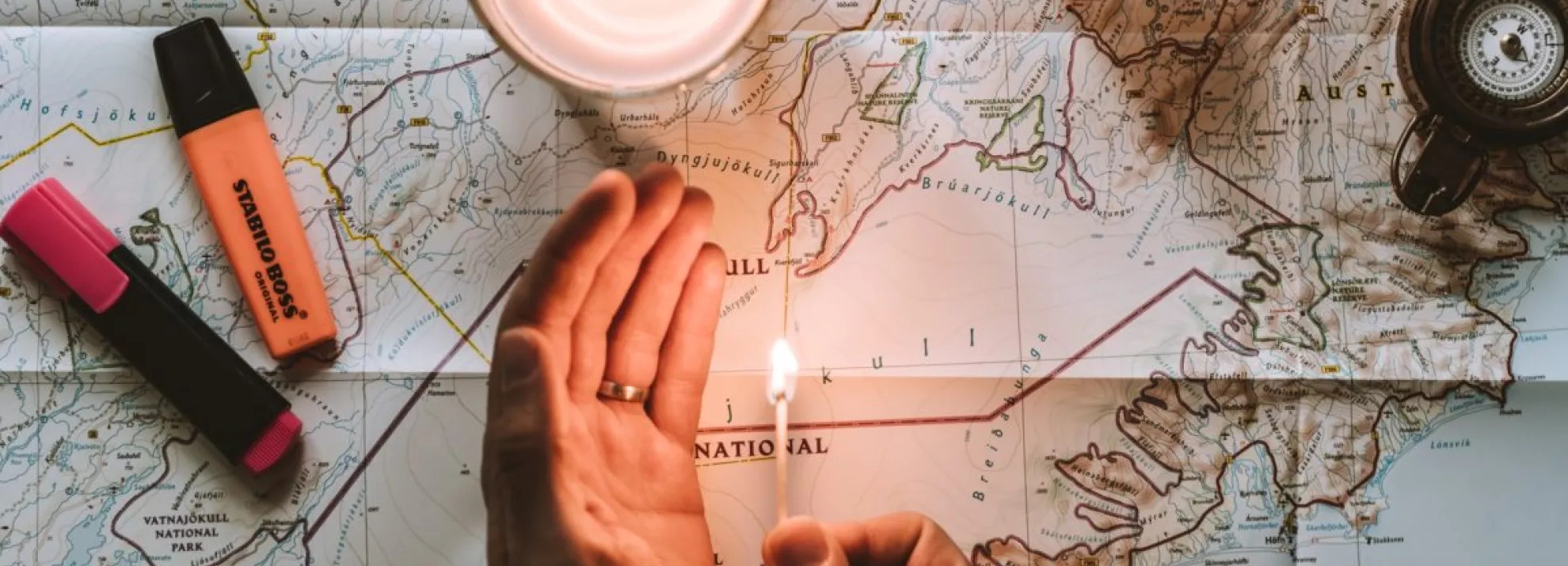 a hand holding a match to a map with candles around it