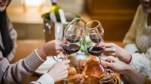 Hands hold glasses of red wine together in a social gesture.