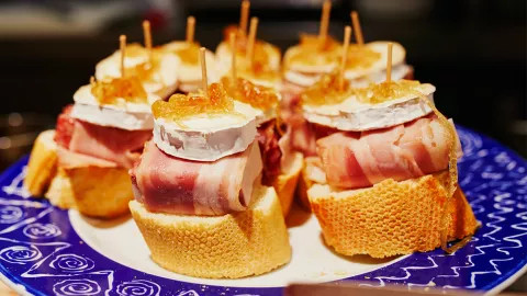 Sliced bread stacked with cheese and meat on skewers sitting on a blue plate.
