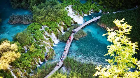 People walking along bridge pathway in Plitvice Lakes National Park in Croatia.