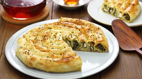 Börek, a savory pastry dish on a plate with a jug of apple tea.
