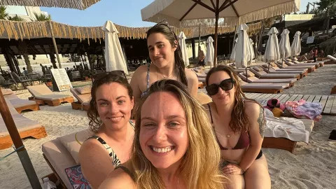 A group of people smiling together while sitting on a sun lounger at the beach.