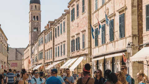 Group of people standing and listening to their trip leader talk in a street in Dubrovnik with the bell tower behind.