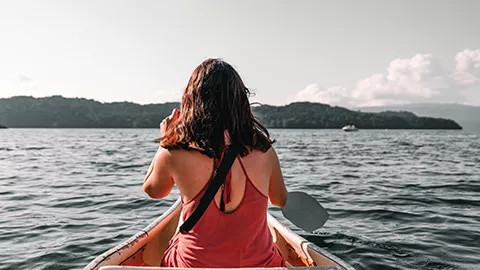 Person from behind, paddling a kayak on water.