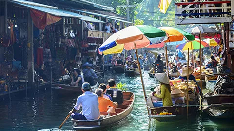 Wooden boat carries passengers down a river towards a floating market.