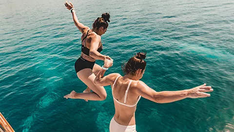 Two people hold hands as they jump from a boat into the ocean.