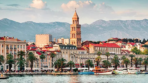 Split’s cityscape with boats docked, palm trees lining the shoreline and mountains in behind.