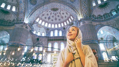 Person wearing a scarf looks up at the detailed roof of the Blue Mosque in Istanbul.