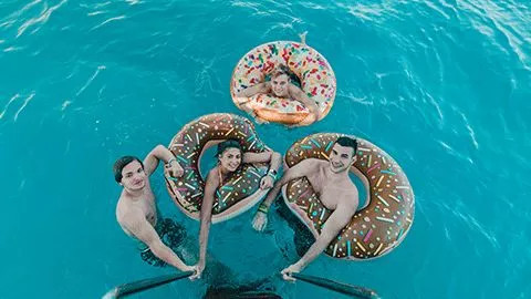 People holding onto the ladder of a boat while floating in donut themed floatation devices.