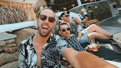 Three people taking a selfie wearing loose button up shirts and sunglasses.