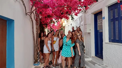 Group of people posing together in traditional white street with pink flowers above them.