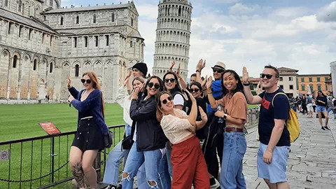 Group of travellers posing together in front of the Leaning Tower of Pisa