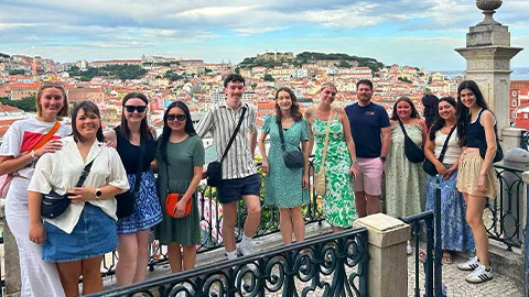 People standing together for a photo on a balcony with a city view behind them.