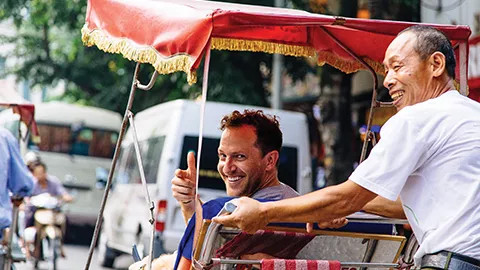 Smiling person in a tuk tuk signals a thumbs up with their hand.