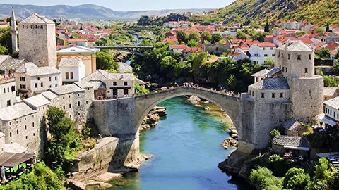 Large stone bridge over blue river with stone buildings on either side.