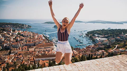 Person jumping with their hands in the air and the city of Hvar behind them.