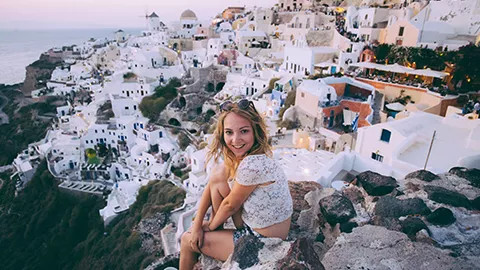 Person sitting down looking over hillside covered in traditional white greek houses.