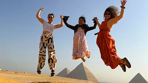 Three people jump in the air in front of the pyramids in Egypt.
