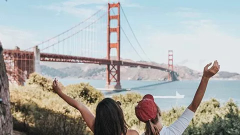 Two people standing with their hands out in the air in front of the Golden Gate Bridge in San Francisco