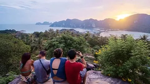 People sitting on a rock lookout while the sun comes up over the Phi Phi islands in Thailand.