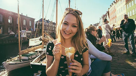 Person holding gelato in a cone next to a canal that has docked boats.