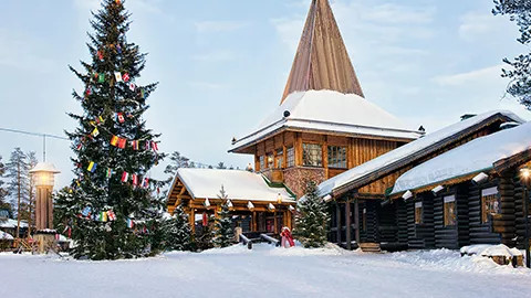 Wooden building covered in snow with a decorated Christmas tree outside.