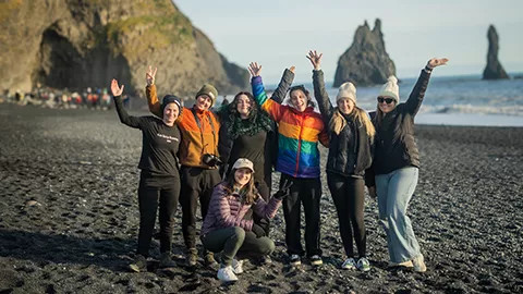 People standing together with their hands in the air on a black sand beach.