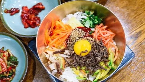 Korean dish Bibimbap with vegetables, rice, egg yolk and sliced meat.