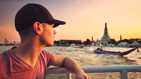Person leaning against a railing near the Chao Phraya River while looking at Wat Arun in Bangkok.