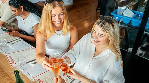 People holding their glasses together in a social gesture while having lunch at a Parisian restaurant.