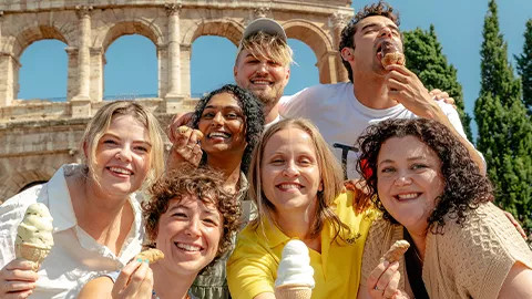 Group of people smiling together while holding gelato and cannoli in front of the colosseum in Rome.