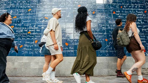 People walking past a blue tiled wall with white writing in Paris.