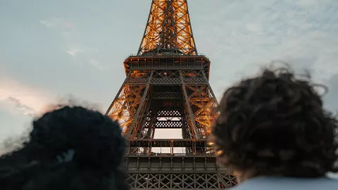 The back of two people sitting side by side with the Eiffel Tower in focus in front of them.