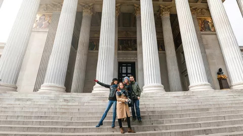 Group of people wearing winter jackets, stand on the steps of the Austrian Parliament Building in Vienna.