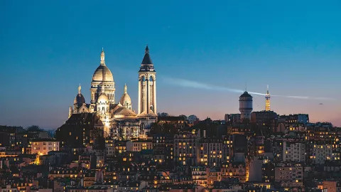 Basilica of the Sacré-Cœur lit up at night with the top of the Eiffel Tower visible to it’s right.