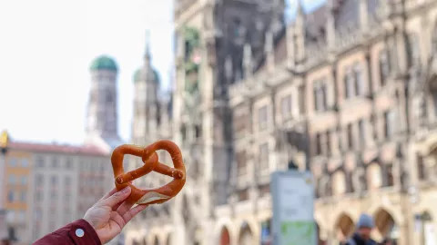 Hand holds German pretzel out in front of the New Town Hall in Munich.