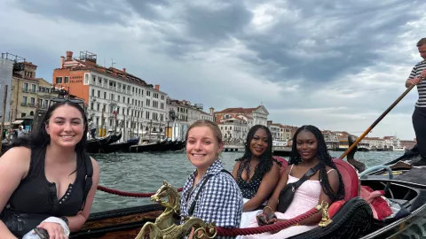 Four people smile together on a gondola boat on the Grand Canal in Venice.