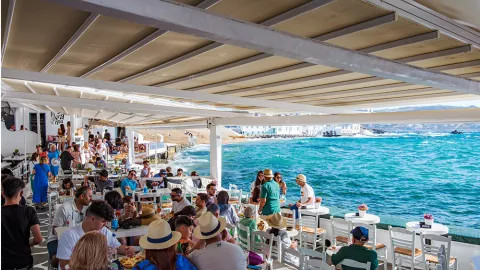 People sitting at tables eating in busy Greek seaside restaurant.