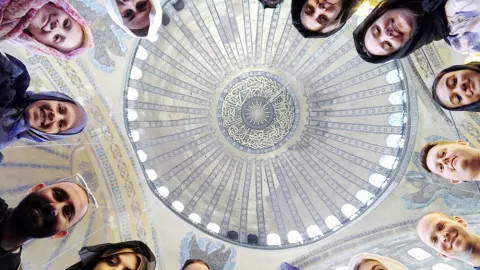 A circle of faces looking downwards with a view of the ceiling of the Hagia Sophia mosque above them.